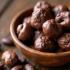 Chocoladebedekte cashewnoten in een houten schaal omringd door cacao bonen en cashewnoten.