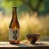 Een fles sake en een traditionele Japanse kop op een houten tafel.