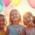 Kinderen glimlachen tijdens een wensvervulling, met kleurrijke ballonnen en decoraties.