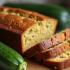 Verse courgettebrood op een houten snijplank met courgettes ernaast.